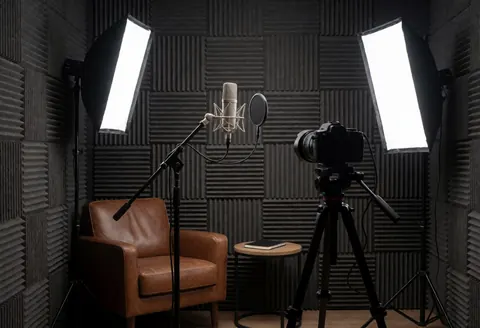 Studio d'enregistrement professionnel équipé d'un microphone, d'une caméra sur trépied, d'un fauteuil en cuir et de lumières, idéal pour les agences marketing et la production audiovisuelle.
