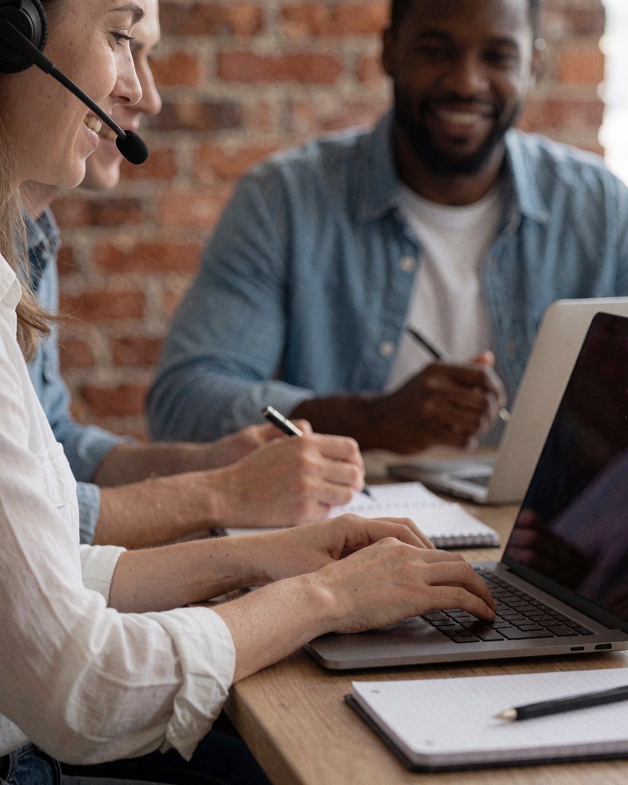 Un homme et une femme collaborent lors d'une leçon en ligne sur un bureau, entourés d'un carnet, d'un stylo et d'un casque audio dans un espace lumineux.