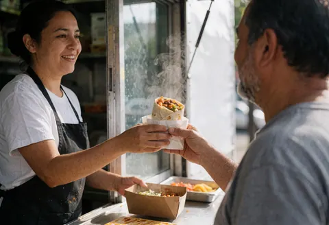 Une vendeuse de street food sert un burrito fumant à un client depuis son camion. L'interaction est chaleureuse, avec un fond flou et une lumière naturelle.