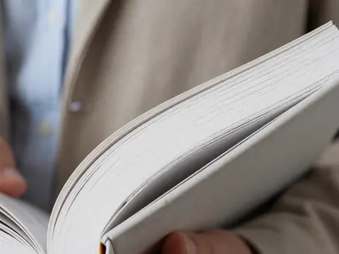 Vue rapprochée des pages d'un épais livre de cours tenu par des mains, illustrant l'étude des langues et la grammaire.