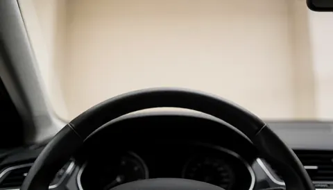 Vue intérieure d'un véhicule montrant un volant noir et un tableau de bord flou, offrant un espace supérieur pour du texte, idéal pour une auto-école.