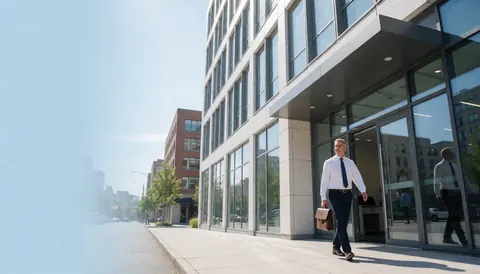 Un comptable marche avec une malletle vers l'entrée d'un immeuble de bureaux moderne sous un ciel bleu dégagé, idéal pour la page d'accueil d'un site web comptable.