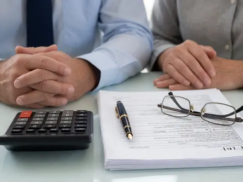 Vue rapprochée d'un bureau avec calculatrice, stylo, lunettes et documents financiers pour services comptables.