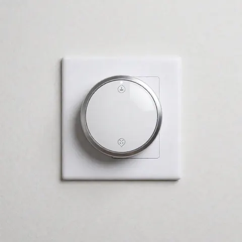 Un thermostat connecté avec écran numérique et boutons métalliques est fixé sur un mur blanc dans une salle de bain au design minimaliste et épuré.
