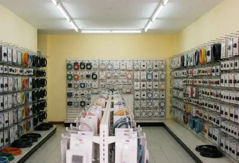Interieur d'un magasin d'electricite avec des etageres remplies de cables, interrupteurs et autres produits electriques. Les murs sont peints en jaune clair et l'eclairage est fluorescent.