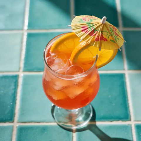 Cocktail tropical garni de tranches de citron et d'un petit parapluie décoratif posé sur des carreaux turquoise, baigné de soleil.