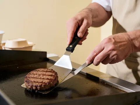 Un hamburger est en cours de cuisson sur une surface de grillage professionnelle, mettant en évidence la préparation culinaire.