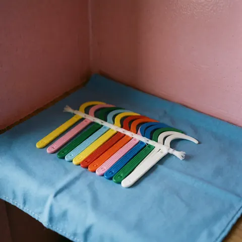 Fil dentaire et cure-dents disposés proprement sur une surface blanche devant un mur rose, illustrant les produits de soins bucco-dentaires.