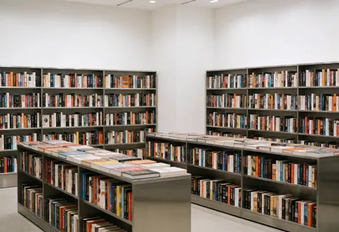 Vue intérieure d'une librairie contemporaine dotée d'étagères métalliques, de murs blancs et de livres disposés géométriquement sous un éclairage vif.
