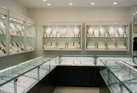 Vue intérieure d'une boutique de bijoux moderne présentant des vitrines éclairées contenant colliers, bagues et boucles d'oreilles en or et argent dans un environnement propre et ordonné.