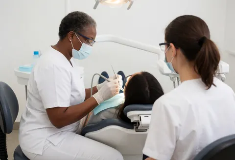 Dentiste en tenue de protection réalise un nettoyage dentaire sur un patient allongé dans un cabinet moderne.