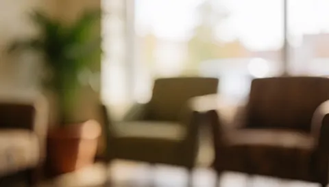 Fond neutre de salle d'attente avec chaises confortables et plante en pot, éclairage chaleureux et flou artistique pour textes ou publicités.