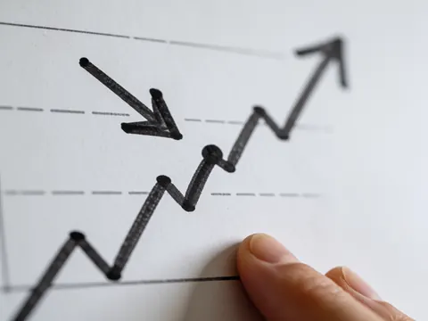 Graphique de tendance ascendante dessiné à la main avec une flèche pointant vers le haut, une main tient le papier sur fond blanc, idéal pour le marketing et les affaires.