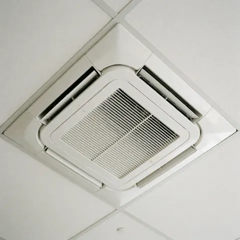 Vue rapprochée d'une unité de climatisation cassette installée dans un plafond blanc, offrant une solution moderne et discrète pour le confort thermique des espaces commerciaux.