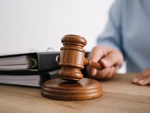 Marteau judiciaire en bois posé sur un bureau, à côté de dossiers de documents juridiques, dans un bureau éclairé par la lumière naturelle.