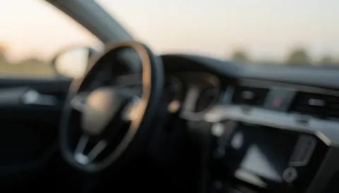 Vue intérieure floue d'un véhicule montrant un volant et un tableau de bord, créant une ambiance calme et professionnelle pour un fond de texte.