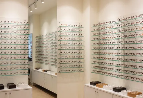 Intérieur moderne d'une boutique d'optique avec présentoirs vitrés, étagères murales et cadres de lunettes disposés pour la vente au détail.