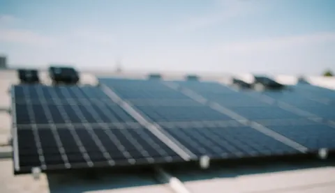 Vue rapprochée d'un toit couvert de panneaux solaires avec un ciel bleu en arrière-plan, servant de fond pour le design web et les textes.