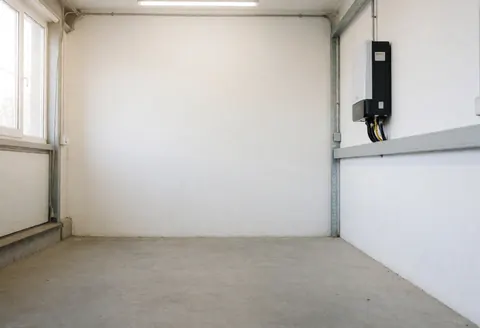 Nouvel onduleur solaire fixé sur un mur blanc dans un atelier vide et bien éclairé avec un sol en béton, idéal pour illustrer des services professionnels d'énergie solaire.