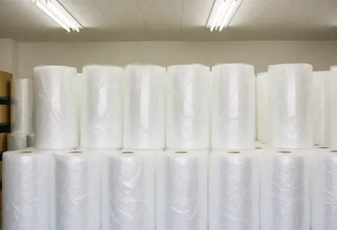 Entrepôt de déménagement avec des rouleaux de film bulle blancs empilés, éclairage fluorescent, environnement propre et organisé pour emballer meubles et objets.
