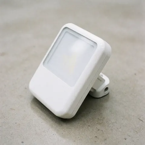 Un projecteur LED blanc au design moderne est fixé sur un mur extérieur en béton gris, assurant un éclairage sécurisé et esthétique pour les bâtiments professionnels.