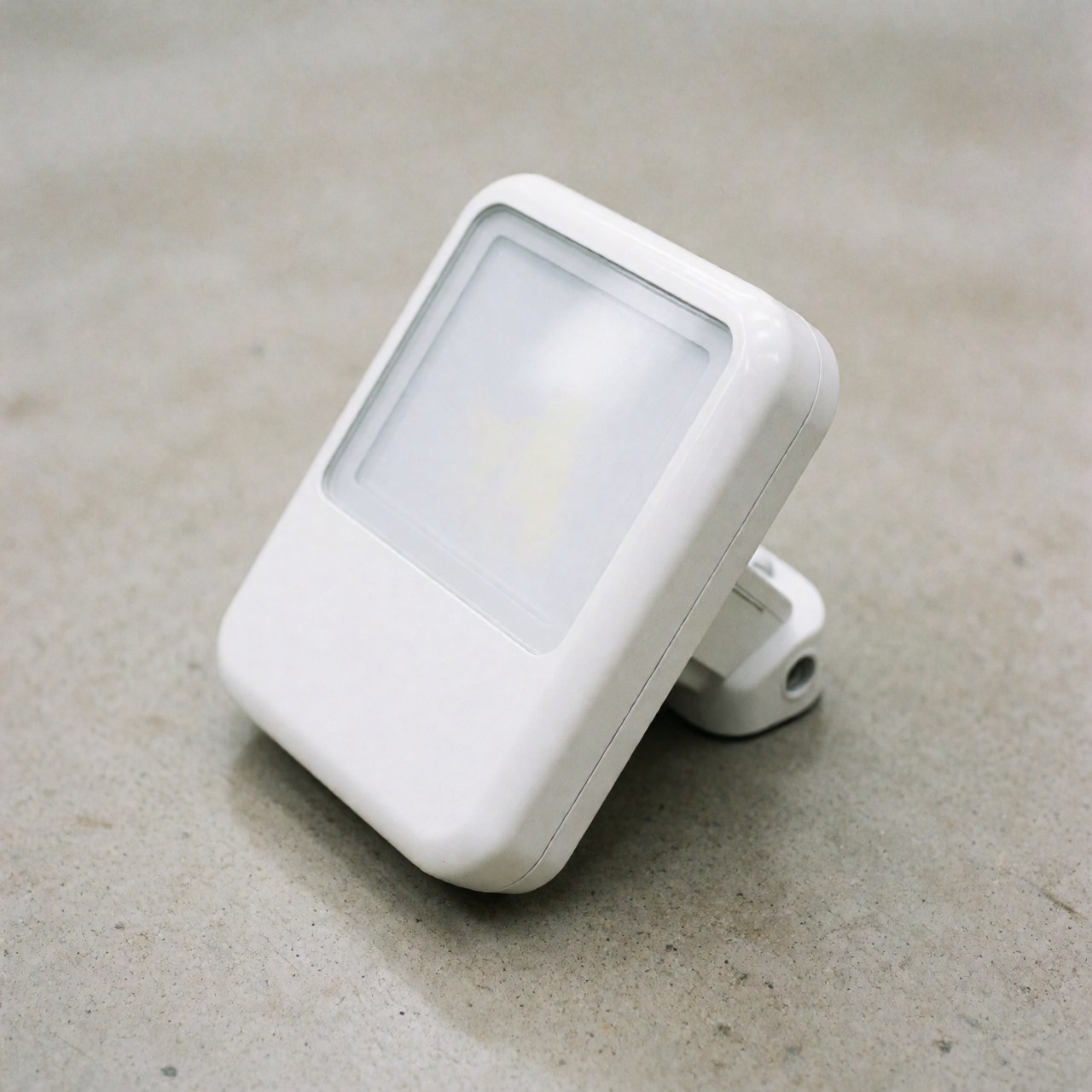 Un projecteur LED blanc au design moderne est fixé sur un mur extérieur en béton gris, assurant un éclairage sécurisé et esthétique pour les bâtiments professionnels.