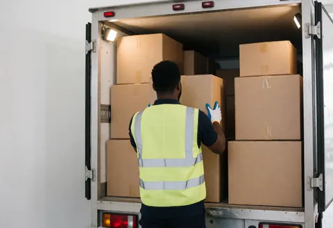 Un déménageur portant gants et gilet réfléchissant organise des cartons à l'arrière d'un camion éclairé par des feux de travail.