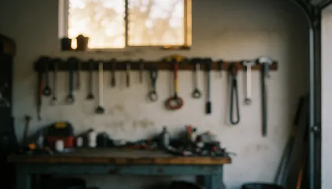 Fond d'atelier montrant des outils accrochés au mur et une table de travail en bois, éclairage chaud et doux, idéal pour superposer du texte commercial.