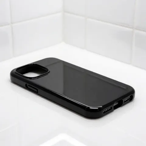 Coque de protection noire pour smartphone posée sur une surface blanche texturée avec des reflets lumineux, évoquant un design moderne et minimaliste pour catalogue ou marketing.