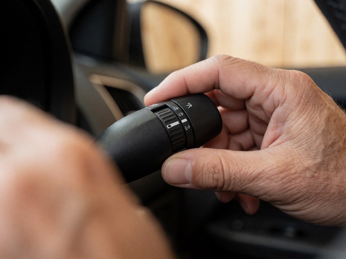 Gros plan sur une main adulte manipulant le levier de contrôle des feux à l'intérieur d'une voiture, avec l'habitacle flou en arrière-plan, pertinent pour la formation à la conduite.