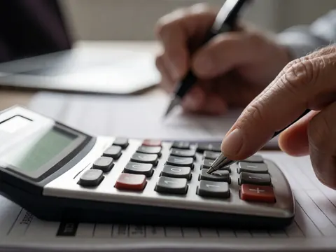 Vue rapprochée d'une calculatrice, d'un stylo et de documents financiers posés sur une surface de travail, évoquant la comptabilité et la gestion précise.