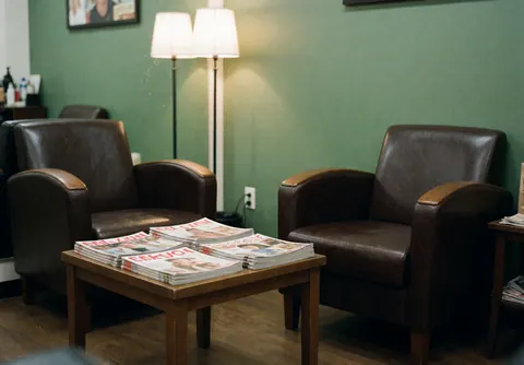 Intérieur d'une salle d'attente vide avec des chaises, une table basse, des magazines et un mur vert dans un salon de barbier.