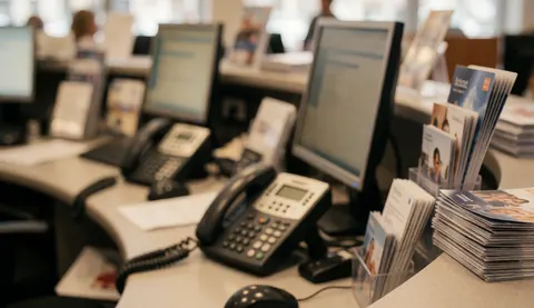 Bureau d'agence de voyages avec moniteurs, téléphones et brochures sur fond flou, idéal pour textes et design web.