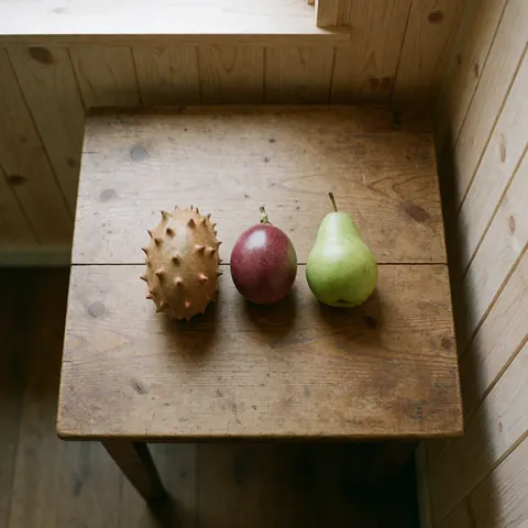 Des fruits locaux riches en fibres disposés sur une table en bois près d'une fenêtre, incluant du kiwano, du fruit de la passion, une poire, dans un intérieur lumineux.