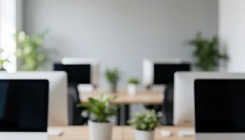 Bureau moderne avec ordinateurs, tables et plantes vertes sur fond flou, idéal pour textes et présentations professionnelles.