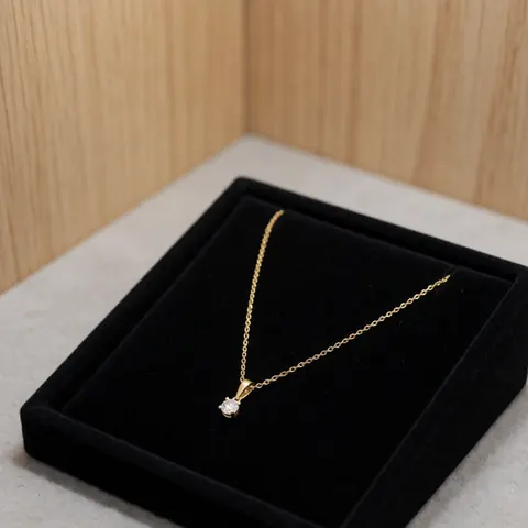 Un collier en or orné d'un diamant est présenté dans une boîte noire sur un fond de bois clair, idéal pour les boutiques de joaillerie.