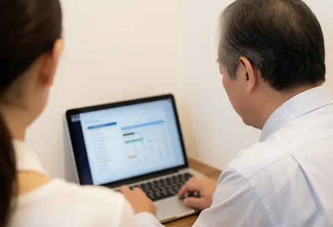 Un entrepreneur examine ses comptes financiers sur un laptop, accompagné d'une femme dans un bureau professionnel aux murs blancs et à l'éclairage chaleureux.