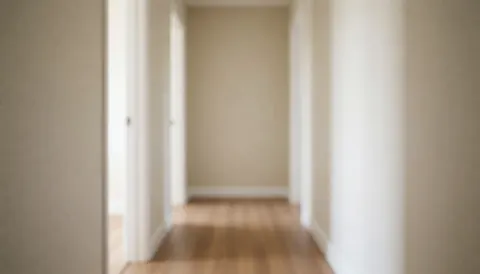 Un couloir intérieur d'une maison avec des murs de couleur beige clair et un plancher en bois, éclairé par une lumière naturelle douce.