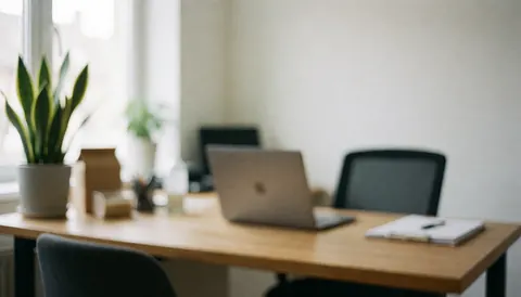 Espace de travail lumineux avec bureau en bois, ordinateur portable, chaise et plante près de la fenêtre, fond flou idéal pour textes.
