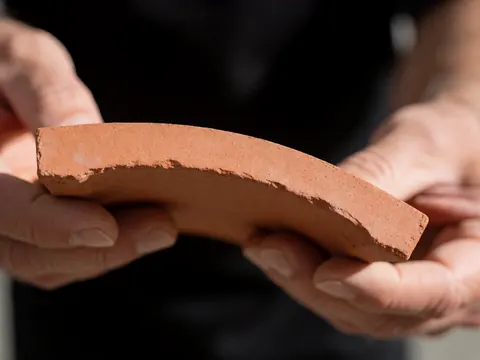 Gros plan sur une tuile en terre cuite de couleur ocre, mettant en valeur sa texture rugueuse et sa forme incurvée typique des matériaux de construction.