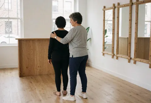Une professionnelle accompagne une cliente lors d'une séance de yoga ou pilates, en ajustant sa posture avec attention dans un studio lumineux et calme.