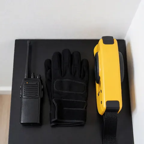 Radio, gants et barrière rétractable disposés sur une surface noire, éléments essentiels pour un catalogue de services de protection.