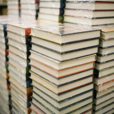 Une pile ordonnée de livres scolaires et universitaires neufs, encore enveloppés dans leur plastique protecteur, prêts pour la vente ou le stockage en librairie.