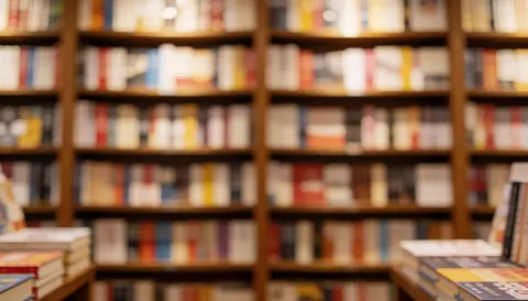 Vue d'arrière-plan floue d'une bibliothèque spacieuse aux étagères en bois, créant une ambiance chaleureuse et calme propice à la lecture.