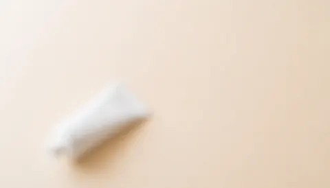 Arrière-plan beige doux et flou avec un tube de crème en coin, idéal pour textes et design web dans les services de beauté.