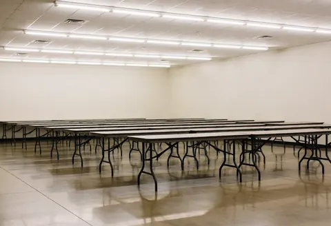 Entrepôt communautaire vide doté de tables métalliques, d'un éclairage fluorescent et d'un sol poli, prêt pour des événements et servant de fond neutre.