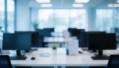 Vue d'un espace de travail contemporain aux tons blancs et bleus, avec des bureaux et des moniteurs légèrement flous servant de fond neutre pour du texte.