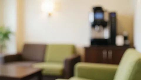 Vue d'un coin repos aménagé avec un canapé confortable, une machine à café et des plantes vertes sur un fond flou chaleureux.