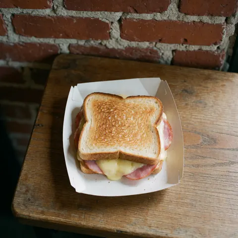 Vue de dessus d'un sandwich au jambon et fromage sur une surface en bois avec un fond en briques rouges.