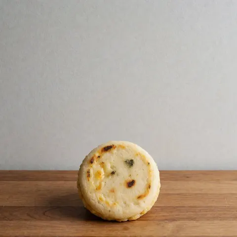 Arepita dorée avec fromage fondu sur une surface en bois, fond gris clair, vue de dessus, style professionnel.